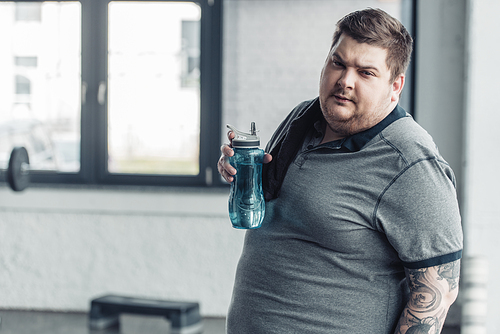 overweight tattooed man  and holding sport bottle at gym