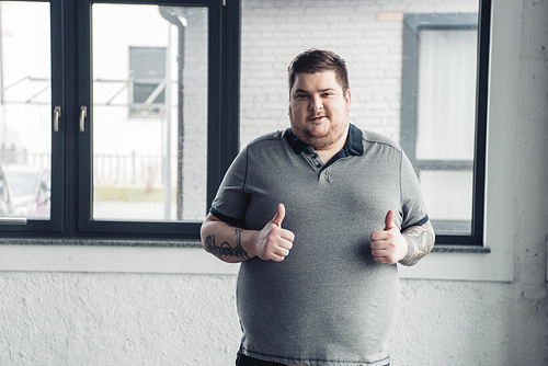 overweight tattooed man in grey t-shirt Looking At Camera and showing thumbs up