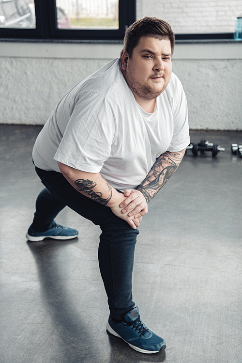 overweight tattooed man  while stretching legs at sports center