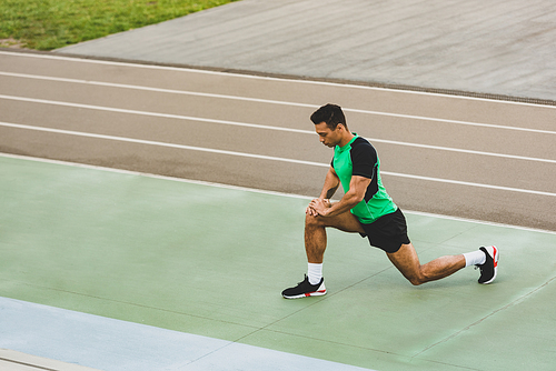 mixed race sportsman in sportswear stretching at stadium