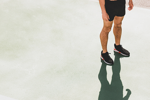 cropped view of sportsman in black sneakers standing at stadium