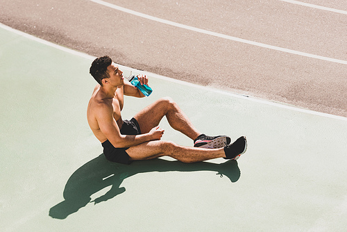 mixed race sportsman sitting at stadium and drinking water