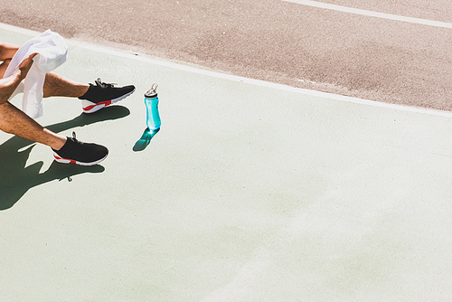 cropped view of sportsman with towel and sport bottle sitting at stadium