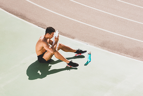 mixed race sportsman sitting at stadium and wiping face with towel