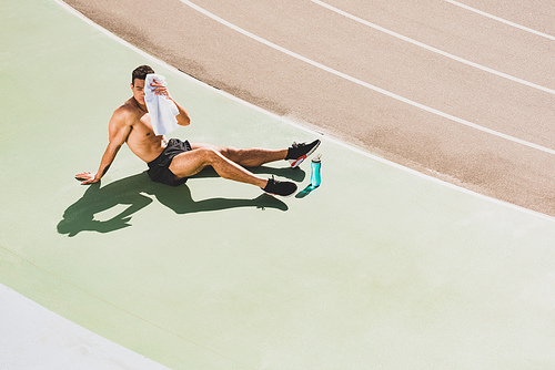 mixed race sportsman sitting at stadium and wiping face with towel