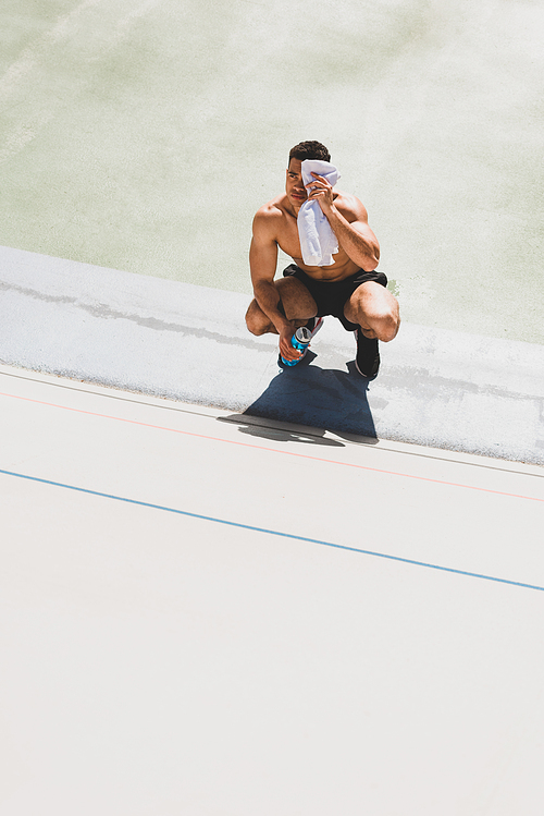 mixed race sportsman sitting at stadium and wiping face with towel