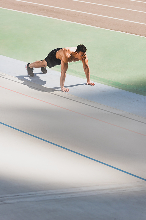 mixed race sportsman standing in plank at stadium