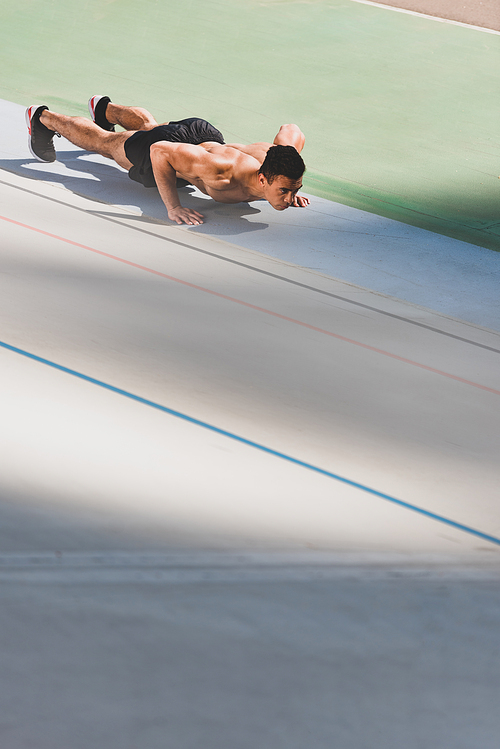 shirtless mixed race sportsman doing push ups at stadium