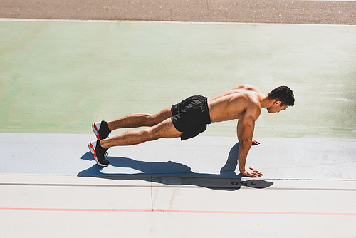 mixed race sportsman standing in plank at stadium