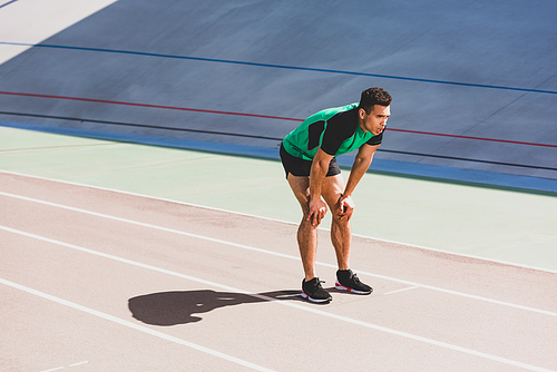 tired mixed race sportsman in sportswear standing at stadium with hands on knees