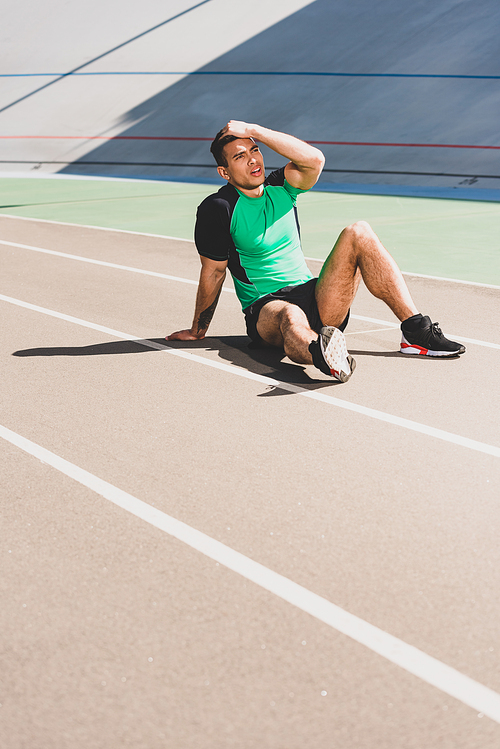 tired mixed race sportsman sitting at stadium and touching head