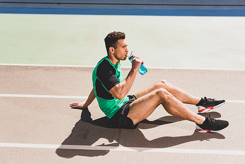 mixed race sportsman sitting at stadium and drinking water