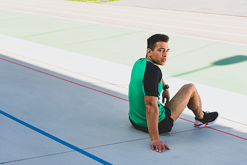 handsome mixed race sportsman sitting on running track and 