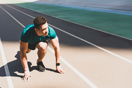 mixed race sportsman on start position looking away at stadium