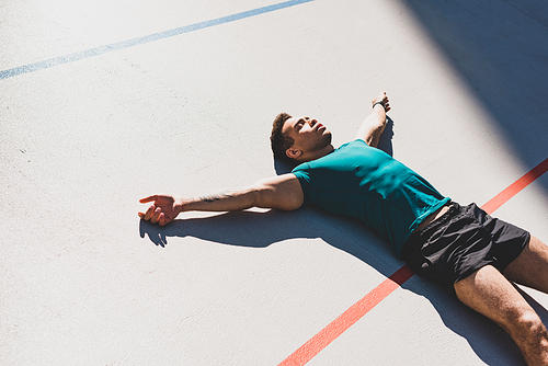 mixed race sportsman laying on running track and spread arms in sunlight