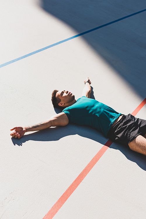 mixed race sportsman laying on running track and spread arms