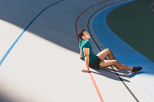 side view of mixed race sportsman sitting on running track at stadium in sunny weather