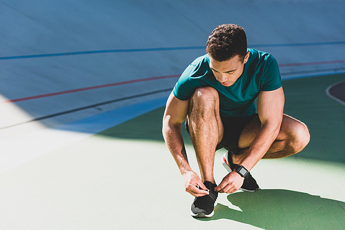 front view of mixed race sportsman lacing up sneakers at stadium