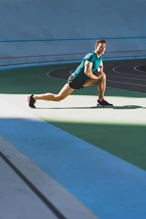 mixed race sportsman doing lunges at stadium, standing on green floor in sunlight