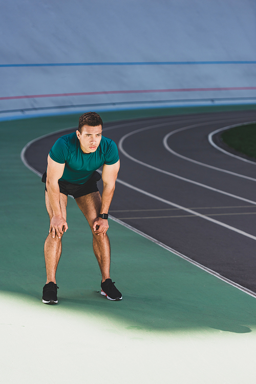 mixed race sportsman with hands on knees standing at stadium