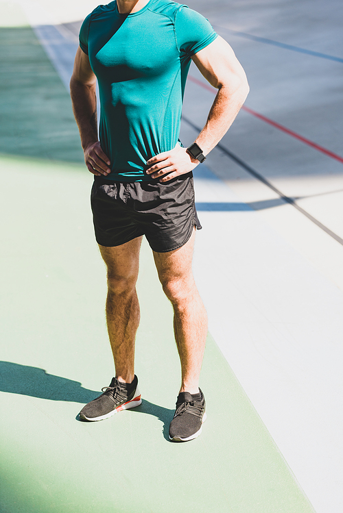 cropped view of sportsman standing with hands on hips at stadium in sunlight