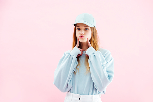 pretty teenage girl in cap grimacing isolated on pink