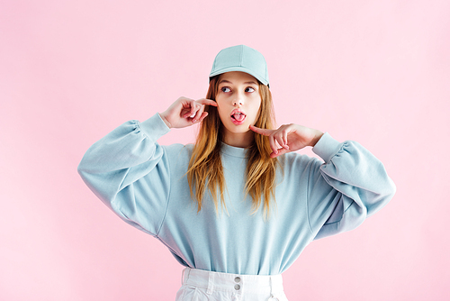 pretty teenage girl in cap sticking out tongue isolated on pink