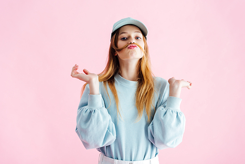 pretty teenage girl in cap with mustache of hair grimacing isolated on pink