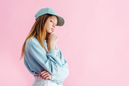 thoughtful sad pretty teenage girl in cap isolated on pink