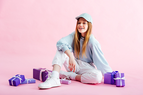 smiling teenage girl sitting near presents on pink