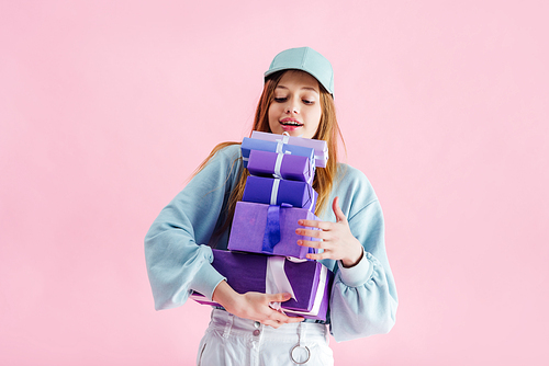 happy pretty teenage girl in cap holding gift boxes isolated on pink