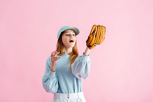 excited pretty teenage girl in cap holding baseball glove isolated on pink