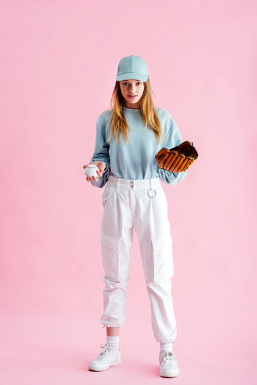 pretty teenage girl in cap holding baseball glove and ball on pink