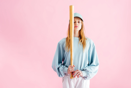 pretty teenage girl in cap holding baseball bat isolated on pink