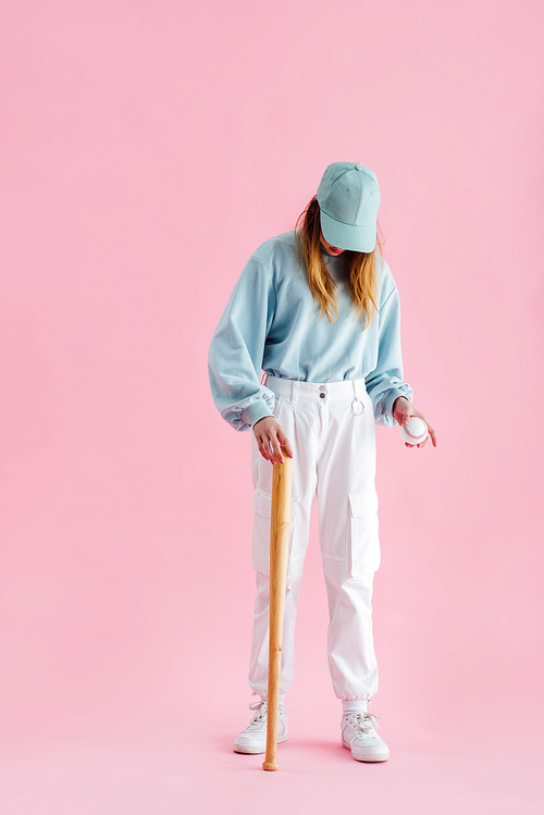 full length view of teenage girl in cap holding baseball bat and ball isolated on pink