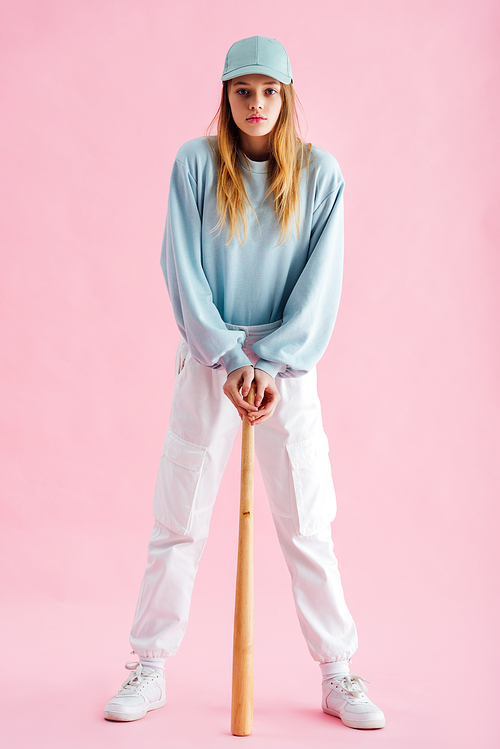 full length view of pretty teenage girl in cap holding baseball bat on pink