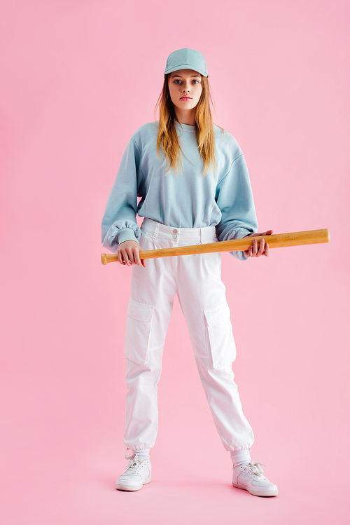 full length view of teenage girl in cap holding baseball bat on pink