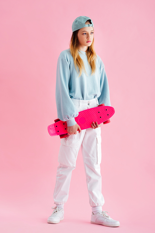 pretty teenage girl in cap holding penny board on pink