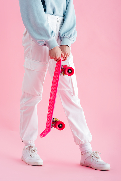 cropped view of teenage girl holding penny board on pink