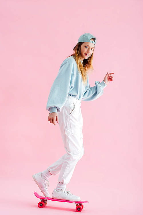 happy pretty teenage girl in cap riding penny board on pink