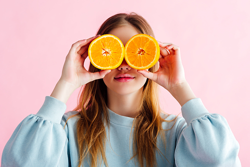 pretty teenage girl holding orange halves in front of eyes isolated on pink