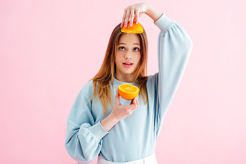 pretty teenage girl looking at orange halves isolated on pink