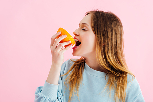 pretty teenage girl with closed eyes biting orange half isolated on pink