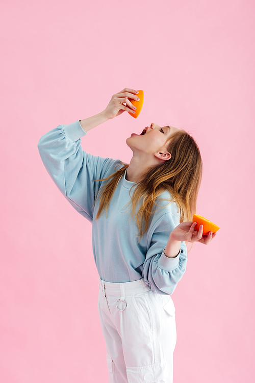 pretty teenage girl squeezing orange juice in mouth isolated on pink