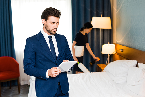 selective focus of handsome man using digital tablet near maid in hotel room