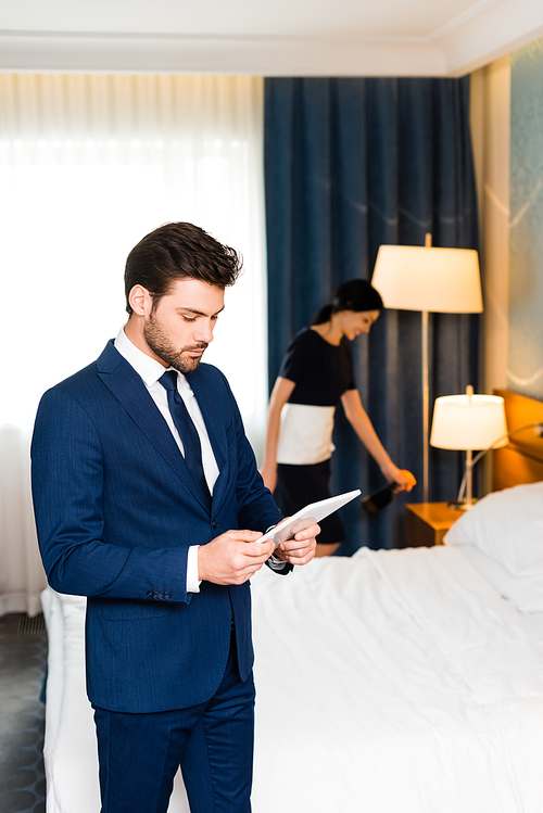 handsome man in suit using digital tablet near maid in hotel room