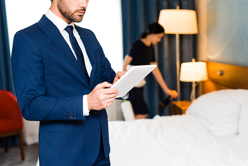 cropped view of man using digital tablet near maid in hotel room