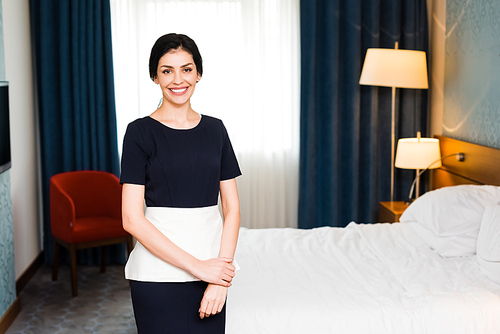 cheerful housemaid smiling while  in hotel room