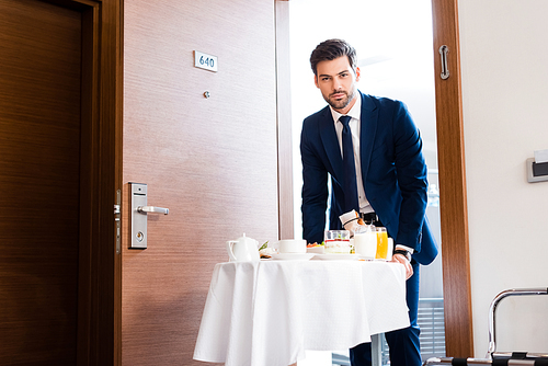 selective focus of handsome receptionist bringing breakfast on food trolley