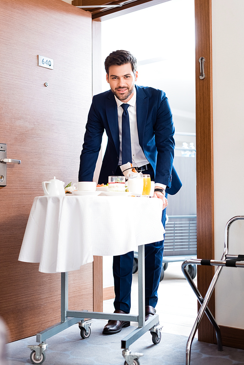 selective focus of cheerful receptionist bringing breakfast on hotel food trolley